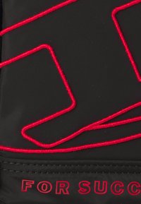 Crni materijal s crvenim izvezenim linijama koje tvore geometrijske oblike. Tekst u debelom crvenom: "ZA USPJEH" na dnu. Glatka tekstura.