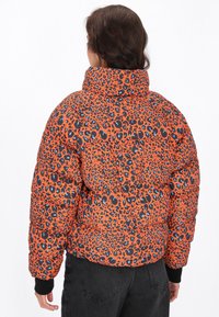 Pufi bunda s designem oranžové leopardí skvrny, s černými a modrými akcenty, vysokým límcem a žebrovanými manžetami. Zobrazeno ze zadní strany.