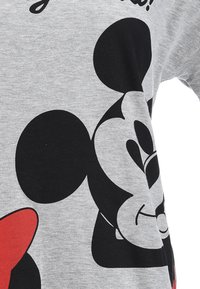 Graues T-Shirt mit einer großen schwarzen Silhouette einem Charakterkopf, verziert mit roten Akzenten und verspielter Typografie über dem Design.