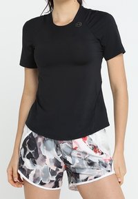 Svart kortärmad träningsoverdel med rund halsringning. I kombination med färgglada, mönstrade shorts med nyanser av grått, rosa och vita accenter.