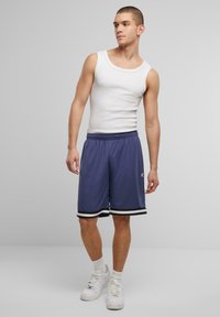 Shorts de sport violets avec des rayures noires et blanches, taille élastique, associés à un débardeur blanc et des baskets blanches.
