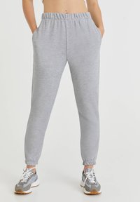 Hellgraue Jogginghose mit elastischem Bund, Seitentaschen, schmal zulaufenden Beinen und gerippten Bündchen. Kombiniert mit grauen Sportschuhen.