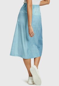 Falda midi de mezclilla azul claro con una forma ligeramente acampanada, que presenta parches de tela en contraste y una cintura elástica para mayor comodidad.
