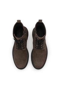 Botines de ante marrón con cordones negros, cremallera y una gruesa suela de goma negra. Presentan una punta redondeada y una lengüeta de talón reforzada.