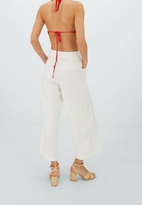 Pantalon blanc à jambes larges avec une taille élastique et des poches latérales, associé à des sandales à talons carrés tressées de couleur noisette et un haut dos nu rouge.