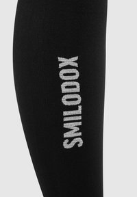 Manicotto elastico nero per gambe con texture a coste, dotato di logo "SMILODOX" ricamato in bianco sul lato.