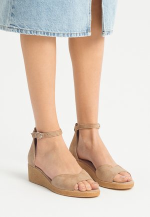 Sandalias de cuña de ante beige con tira en el tobillo, diseño de punta abierta, tacón de cuña texturizado y superficie lisa.