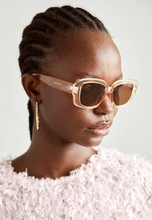 Occhiali da sole oversize beige con montatura trasparente e lenti marroni sfumate, caratterizzati da sottili accenti floreali e un design geometrico audace.