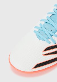 White athletic shoe with a structured textured upper, light blue laces, black accents, and an orange sole.