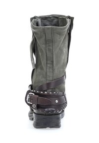 Botín de tobillo de cuero verde con un acabado desgastado, que presenta una correa de cuero marrón y herrajes plateados, además de un tacón apilado. Cierre con cremallera en la parte posterior.