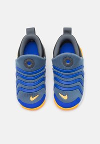 Zapatillas deportivas azul y gris de tipo slip-on con un diseño texturizado ondulado, que presentan detalles en naranja y un logo redondo en la lengüeta. Parte superior de tela suave.