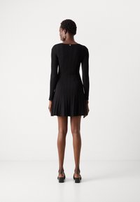 Vestido preto de malha com corpete ajustado e saia rodada, apresentando um relevo texturizado, mangas longas e decote redondo.