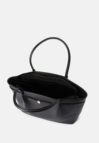 Bolso tote de cuero negro con dos asas largas, parte superior abierta y un bolsillo exterior; cuenta con una superficie texturizada y un diseño minimalista.
