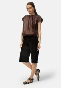 Pruun puff-sleeve top, millega on sobitatud mustad puuvillased culottid ja zebra-halli mustriga korterid. Riietus rõhutab sirgeid jooni ja kontrastseid tekstuure.