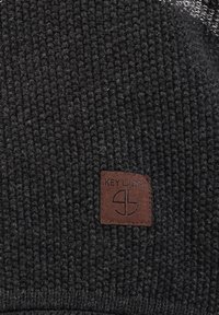 Czarna dziana czapka beanie z fakturowanym wzorem. Posiada brązową skórzaną metkę z logo, przeszytą na przodzie, aby zidentyfikować markę.
