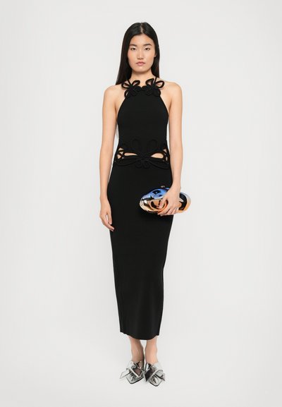Rochie neagră cu guler halter, prezentând decupaje decorative, o siluetă ajustată și accente florale stratificate la decolteu și talie. Plic argintiu.
