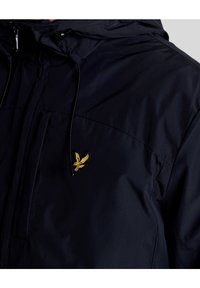 Veste bleu marine foncé avec capuche, fermeture éclair frontale et logo aigle brodé jaune sur la poitrine.