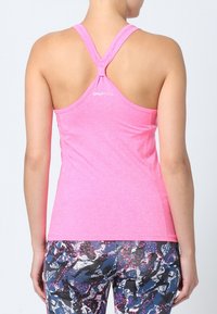 Top da allenamento rosa aderente con design a schiena scoperta, realizzato in tessuto leggero. Abbinato a leggings a fantasia colorati con accenti neri e blu.