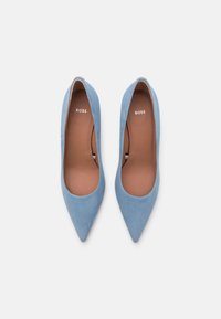 Blå mockaskor med hög klack och spetsig tådesign, med en slät textur och en vadderad beige sula. "BOSS"-logotyp synlig inuti.