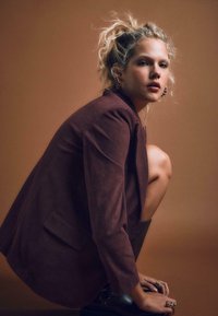 Ruskea corduroy-takki, jossa on ryhdikkäät olkapäät, yhdistettynä polvipitkään mustaan nahkasaappaaseen. Mallin hiukset on muotoiltu löysiksi kiharoiksi.