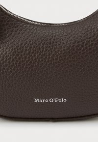 Prim-plan al unei genți din piele maro închis, cu textură, fermoar argintiu și logo Marc O'Polo inscripționat alb.