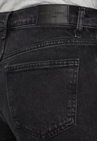 Los jeans de mezclilla gris oscuro presentan una textura suave, un corte ajustado y una etiqueta de cuero que dice "DENIM PREMIUM" en la parte trasera de la cinturilla.
