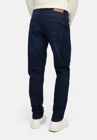 Dark blue denim jeans with a slim fit, featuring two back pockets, contrast stitching, and a brown leather patch on the waistband.