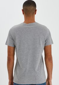 Camiseta gris de manga corta con cuello redondo, hecha de tela suave, presenta un diseño sencillo y un corte holgado, mostrada desde la parte de atrás.