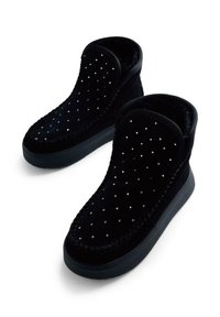 Botas de ante negras con un diseño de caña alta, adornadas con tachuelas plateadas y una suela negra texturizada para un mejor agarre.