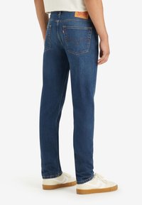 Blå denimjeans med rak passform, som har två bakfickor, en strukturerad midja och en brun läderetikett bak.