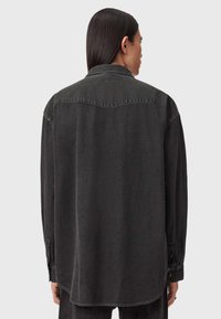 Czarna koszula dżinsowa o lekko luźnym kroju, z kołnierzykiem w kształcie szpicy, długimi rękawami i mankietami zapinanymi na guziki. Gładka tekstura i zaokrąglony dół.