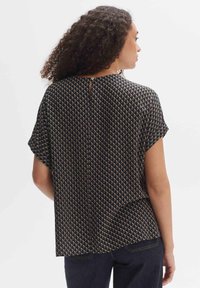 Blusa nera a maniche corte con un motivo geometrico in oro e bianco, con dettaglio della schiena a chiave e una vestibilità rilassata.