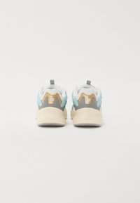Sportskor med en vit mesh-överkropp, aqua- och gråa detaljer, beige sula och en texturerad baksida med en dragflik.