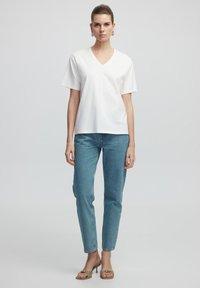 T-shirt bianca a collo a V con maniche corte abbinata a jeans in denim azzurri. Modella che indossa sandali beige e orecchini a cerchio argentati.