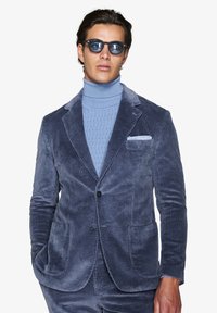 Marinblå kordfløyelsblazer med skräddarsydd passform, två framfickor, slagkrage och kombinerad med en ljusblå rullekrage-tröja.