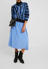 Blå och svart randig tröja över en plisserad ljusblå kjol, i kombination med svarta läderankelstövlar och en texturerad svart handväska.