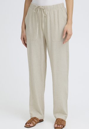 Beige linnedragtnederdel med snøre, frontlommer, båret med brune flade sandaler på en person, der står mod en ensfarvet baggrund.