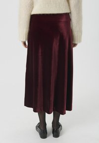 Falda midi de terciopelo burdeos con una textura suave, forma fluida y una cinturilla elástica, combinada con zapatos negros y medias.