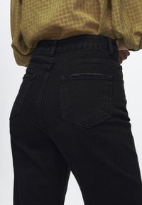 Jeans en denim noir au design ajusté, présentant une taille haute, deux poches au dos et un léger effet usé sur les bords.