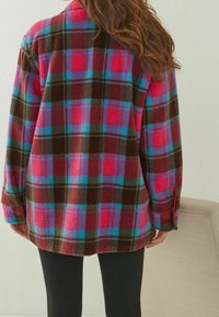 Hřejivá, nadměrná flanelová košile v růžové, fialové a tyrkysové kostce s hnědými akcenty; má knoflíkové manžety a uvolněný střih.