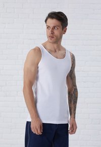 Fehér pamut ujjatlan felső kerek nyakkivágással és széles vállpántokkal, fittebb fazonban, látható izomdefinícióval.