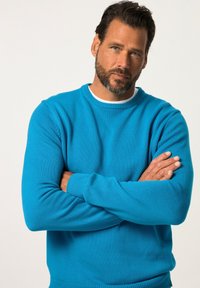 Blauer Strickpullover mit Rundhalsausschnitt und gerippten Bündchen und Saum. Der Stoff wirkt weich und strukturiert, ideal für legere Outfits.