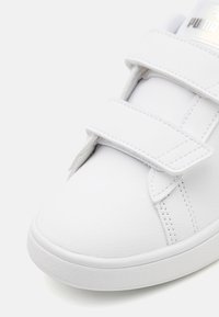 Witte leren sneaker met een gladde textuur, voorzien van twee verstelbare klittenbandsluitingen en een ronde neus. Subtiele stikseldetails.