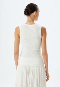 Witte geribbelde tanktop met een ronde halslijn en mouwloos ontwerp, gecombineerd met een vloeiende witte rok. De achterkant toont een getailleerd silhouet.