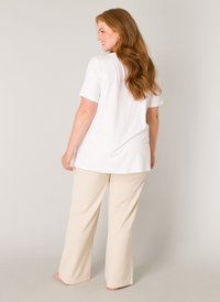 Witte T-shirt met korte mouwen gecombineerd met beige wijde broek. Zachte stof met een comfortabele pasvorm. Model gezien van achteren met lang haar.