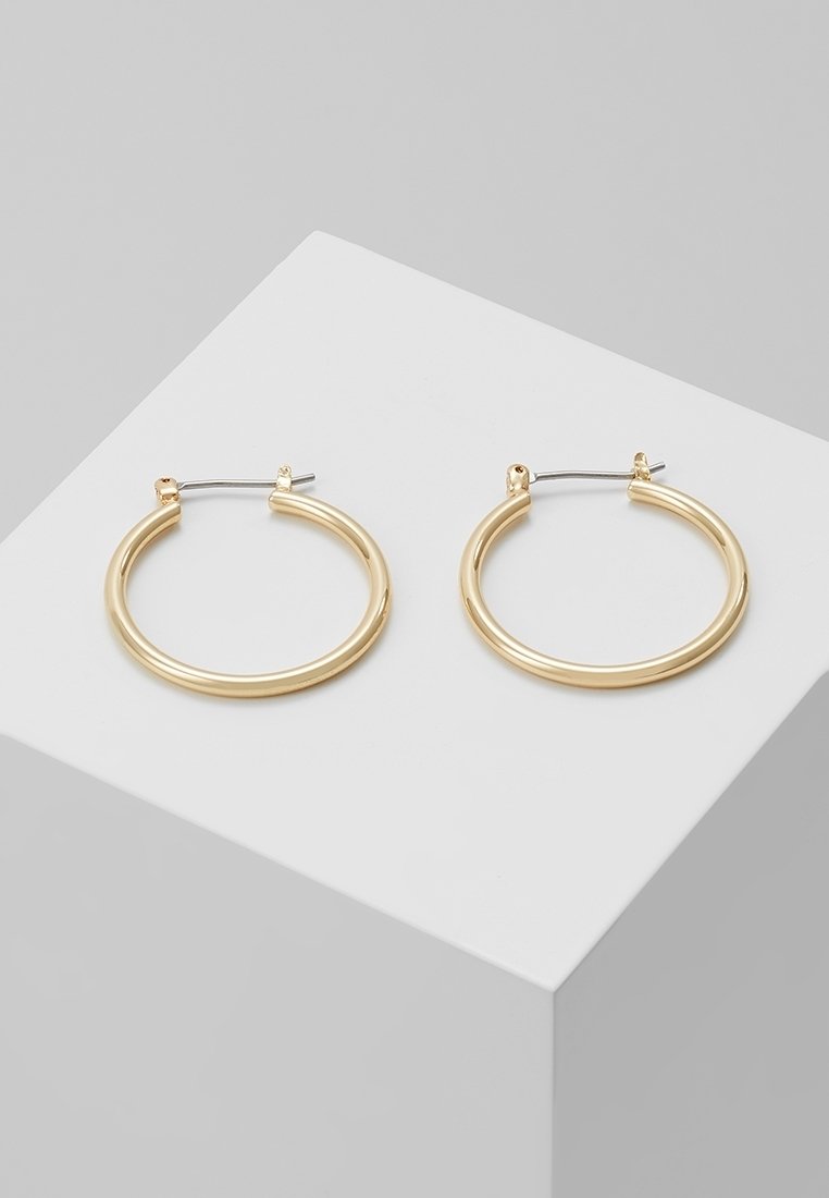 Paire de boucles d'oreilles créoles simples en or avec fermoirs en argent posées sur une surface blanche inclinée sur fond gris.