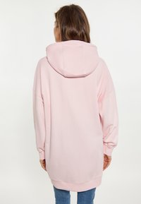 Sudadera rosa de gran tamaño con una capucha grande, hombros caídos y puños de canalé. Tela suave con un ligero brillo. Vista trasera, combinada con jeans azules.