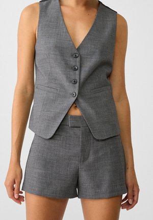 Grijze vest met een diepe V-hals, vijf knopen en twee zijzakken, gecombineerd met bijpassende op maat gemaakte shorts, beide in een textiel met structuur.