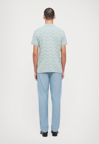 Cămașă scurtă, de culoare albastru deschis, cu modele mici și pantaloni din material similar, cu dungi fine albastre, purtată cu pantofi negri. Văzută din spate.