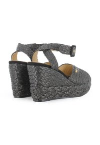 Sandalias de cuña tejidas en negro con diseño de tiras cruzadas, interior acolchado y tacón elevado. Textura suave y detalles en dorado.